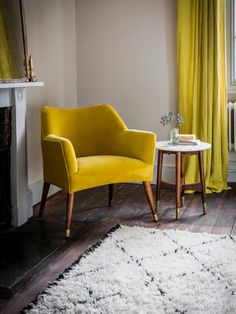 a yellow chair sitting next to a white table on top of a wooden floor in front of a window