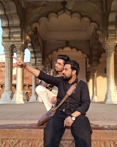 two men sitting on a wall pointing at something