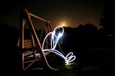 a swing at night with light painting in the foreground and trees in the background