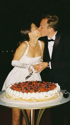 a man and woman kissing in front of a cake with berries on it at night