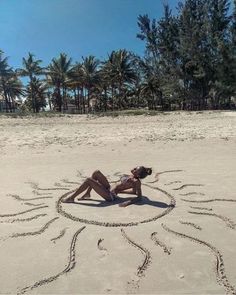 a woman laying on top of a sandy beach next to palm trees and writing in the sand