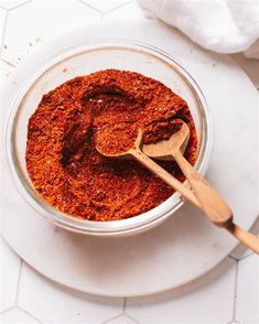 a glass bowl filled with spices on top of a white tablecloth next to a wooden spoon