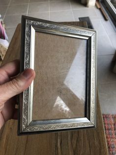 a person holding up a silver frame on top of a wooden table