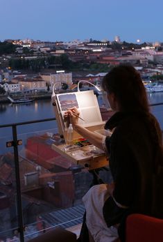 a woman sitting at a table with a laptop on top of it, in front of a cityscape