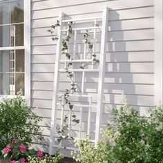 a white ladder leaning against the side of a house with pink flowers in front of it