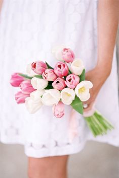 a bouquet of tulips and other flowers is held by a woman in a white dress