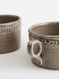 two silver mugs sitting next to each other on a white surface with an elephant head in the middle