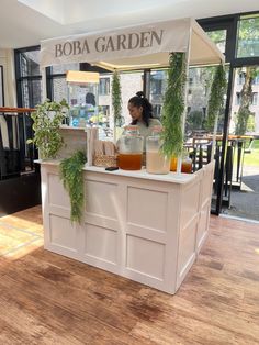 a woman standing behind a counter filled with juices and drinks in front of a window