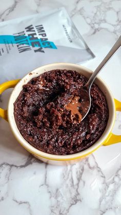 a bowl of chocolate pudding with a spoon in it next to a bag of protein powder