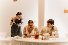 a bride and groom laugh as they sit at a table with drinks in front of them