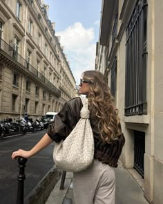 a woman is walking down the street with a purse on her shoulder and she has long curly hair