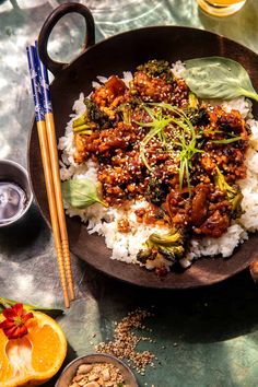 a plate with rice, meat and vegetables on it next to chopsticks and orange slices