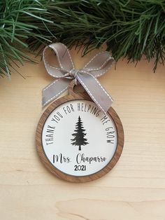 a christmas ornament hanging from a pine tree with a ribbon on it's side