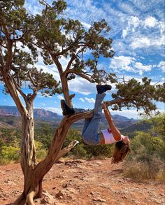 a woman hanging upside down from a tree in the middle of a dirt field with mountains in the background