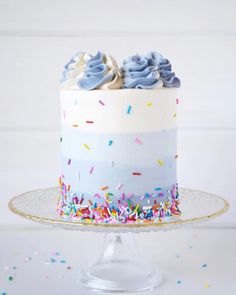 a birthday cake with sprinkles and frosting on a glass stand against a white background