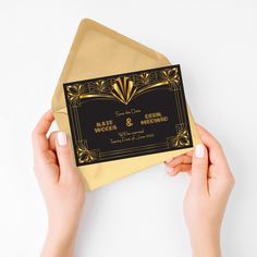 two hands holding an envelope with a black and gold wedding card