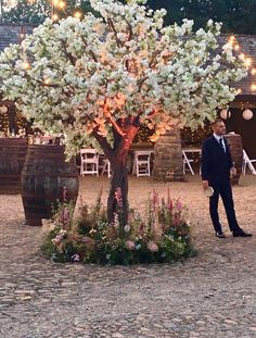 a man in a suit standing next to a tree with white flowers and lights on it