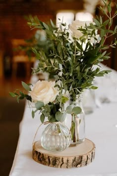 flowers are in vases on a table with white linen and greenery, along with candles