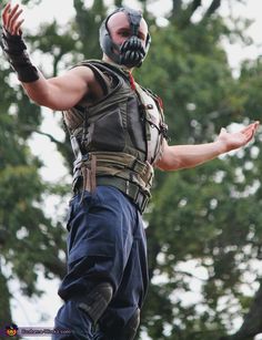 a man dressed as the dark knight rises in front of some trees with his arms outstretched