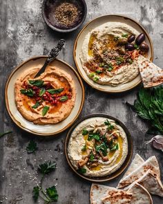 three plates with hummus, olives and other food items on top of them