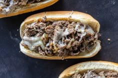 two open sandwiches with meat and cheese on them sitting on top of a black surface