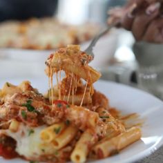 a white plate topped with pasta covered in sauce and cheese being held by a fork