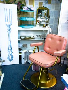 a pink chair sitting on top of a metal stool next to a white table and shelves