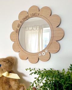 a teddy bear sitting in front of a mirror on a shelf next to a potted plant