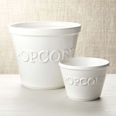 two white cups sitting next to each other on top of a wooden table with the word popcorn printed on them