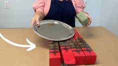 a woman in an apron is holding a pan on top of some red and green boxes