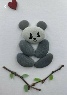 a panda bear sitting on top of some rocks next to a tree branch with a red heart