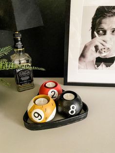 there are pool balls in a tray next to a framed photo and a bottle of booze