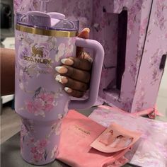 a person holding a pink coffee cup with flowers on it and the words stanex in gold lettering