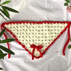 a red and white crocheted triangle on top of a white sheet with green leaves