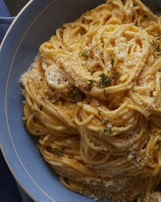 a blue bowl filled with pasta covered in parmesan cheese and garnished with herbs