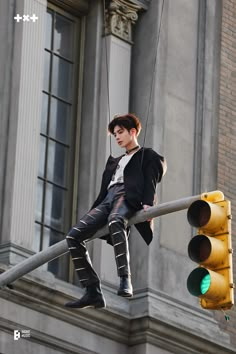 a man hanging from a traffic light with his legs in the air while wearing black boots