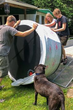 three people and a dog are working on a large object in the grass with another person standing next to it