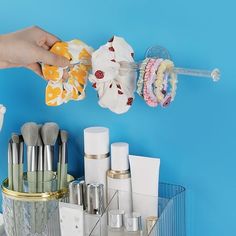 a person is holding up some makeup brushes and other items on a blue wall behind them