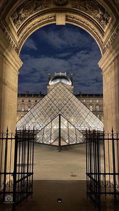 the pyramid is lit up at night in front of an ornate gated area with wrought iron railings