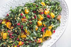 a white plate topped with spinach salad and oranges on top of a table