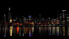 the city skyline is lit up at night with bright lights reflecting in the water and dark skies