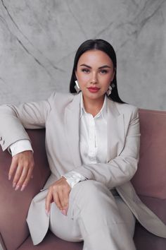 a woman sitting on top of a couch wearing a white suit and silver earrings in front of a marble wall