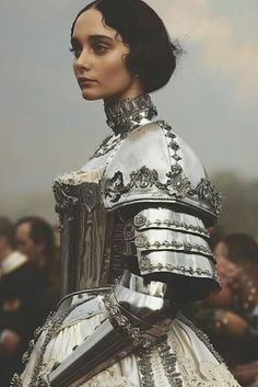 a woman in a silver and white dress is looking off into the distance with people behind her