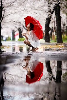 a woman kneeling down in the rain with an umbrella over her head, holding a red umbrella