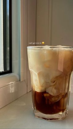 a cup filled with liquid sitting on top of a white counter next to a window