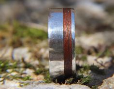 a wooden ring with silver and red inlays on top of some mossy rocks