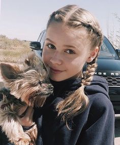 a woman holding a small dog in front of her face and looking at the camera