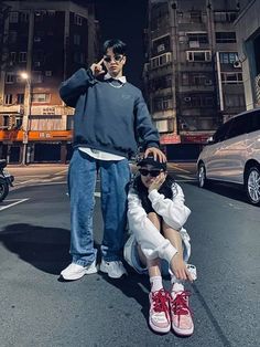 a man and woman sitting on the ground next to each other in front of some buildings