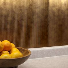 a wooden bowl filled with oranges on top of a counter