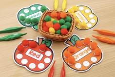 an orange and green basket filled with apples next to carrots on top of a wooden table